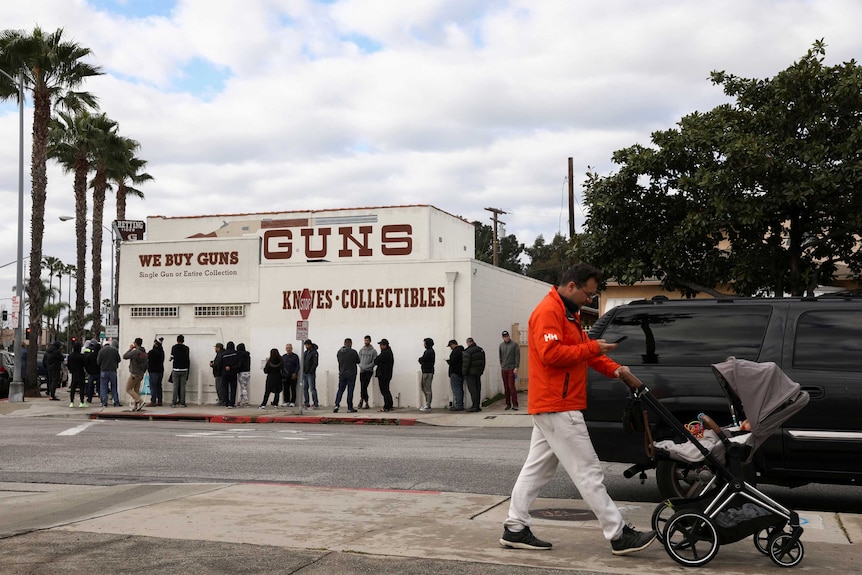 A pedestrian pushes a stroller as people wait in line outside to buy supplies at the Martin B Retting, Inc gun store