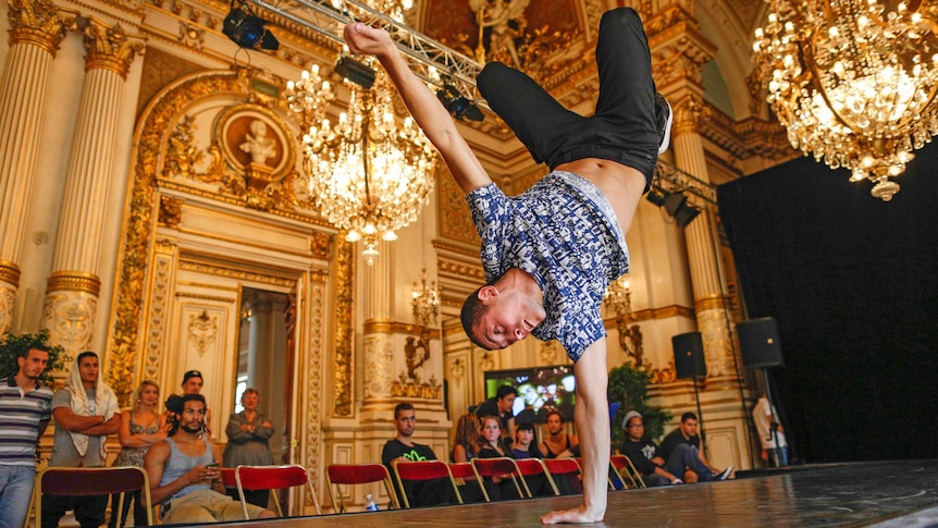 A man leaning on his left hand with his right hand and body in the air, as he break dances.