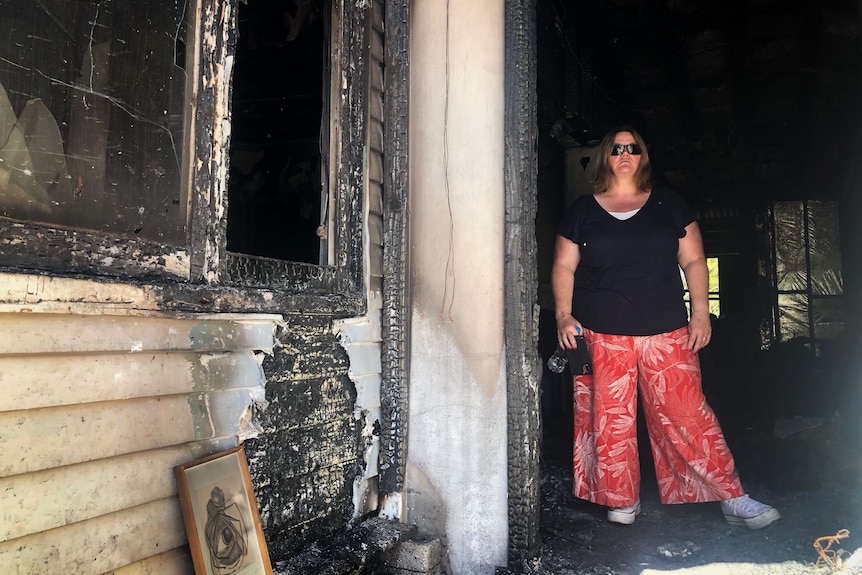 A woman standing at the doorstep of a burnt down house.
