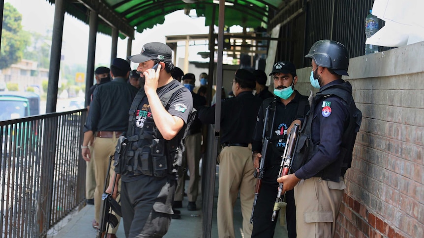 Police officers hold guns and gather at an entry gate of a district court. One speaks into a mobile phone.