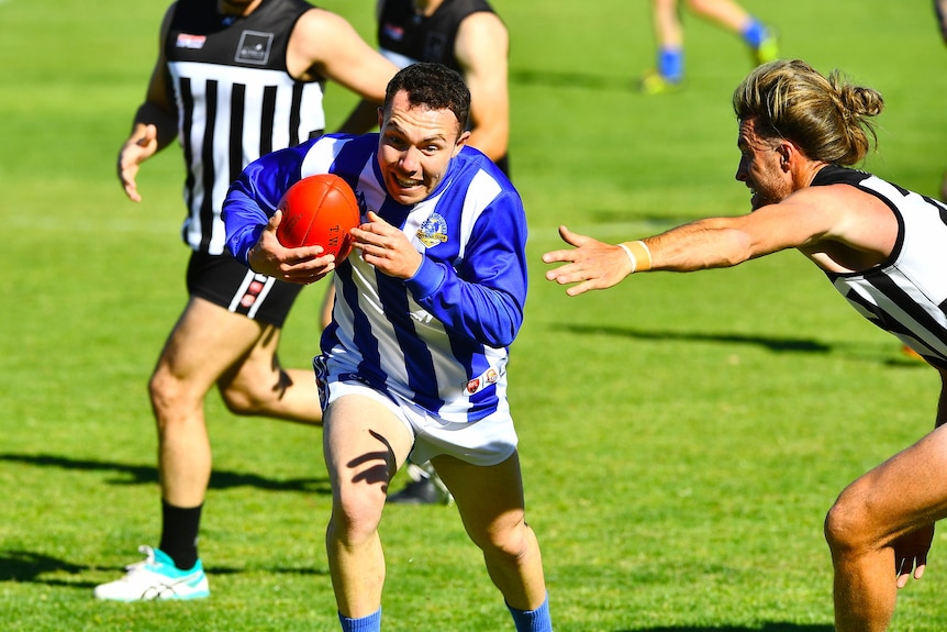 A man wearing a blue and white football jumper runs past a man wearing a black and white football jumper.