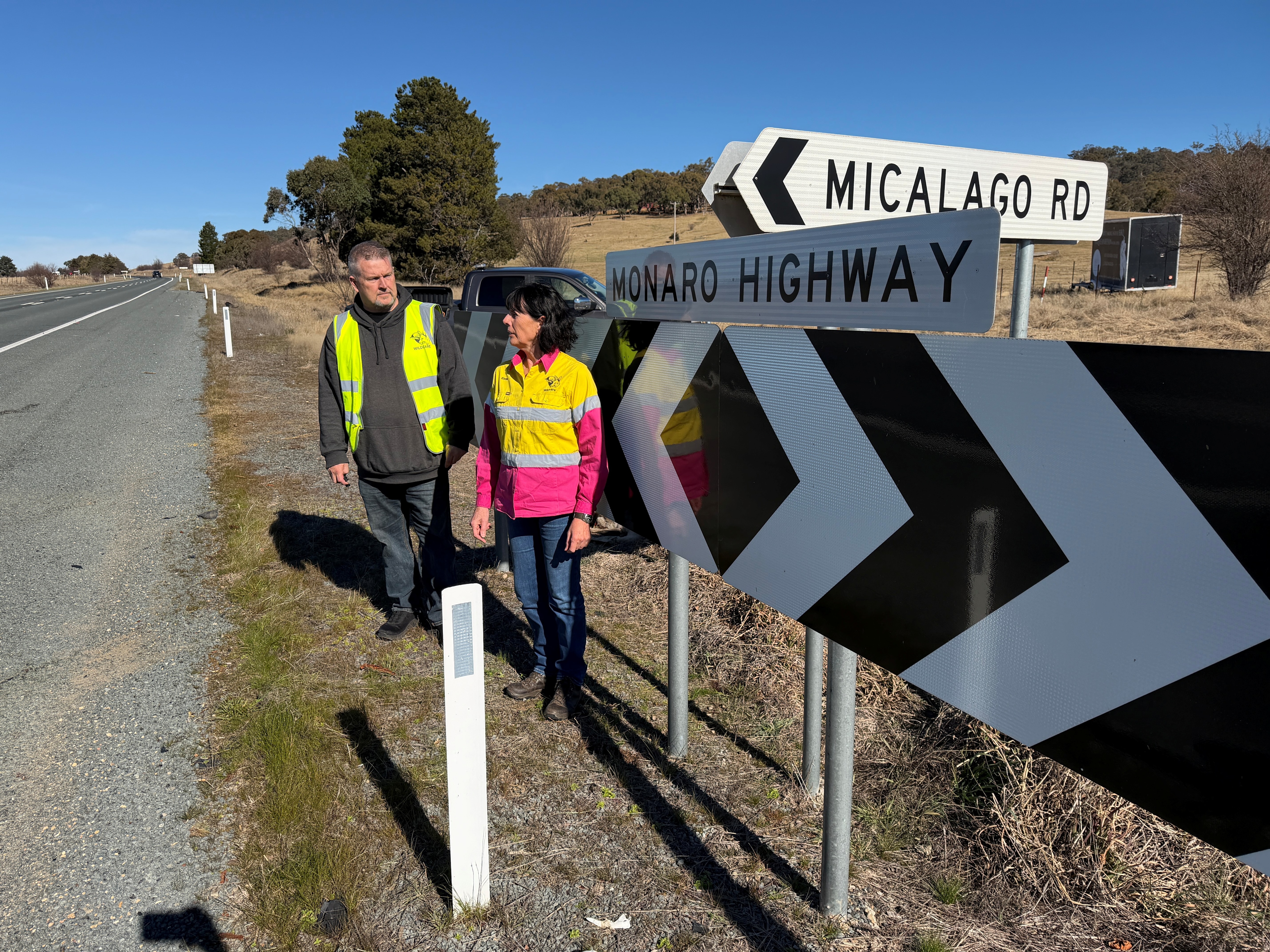 Two people standing in front of a road sign that says Monaro Highway