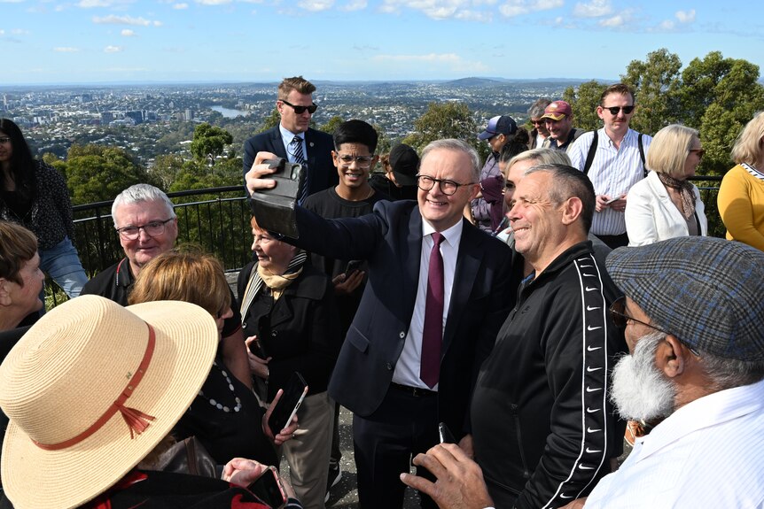 Anthony Albanese smiling and taking a selfie with a voter, surrounded by people at the Mount Coot-tha lookout.