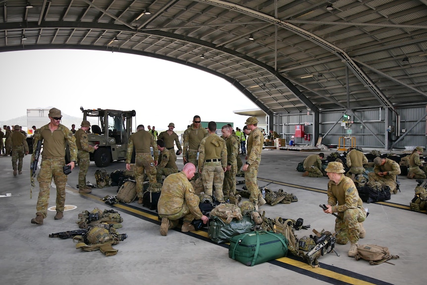 Army personnel pack bags and weapons in an aircraft hangar 