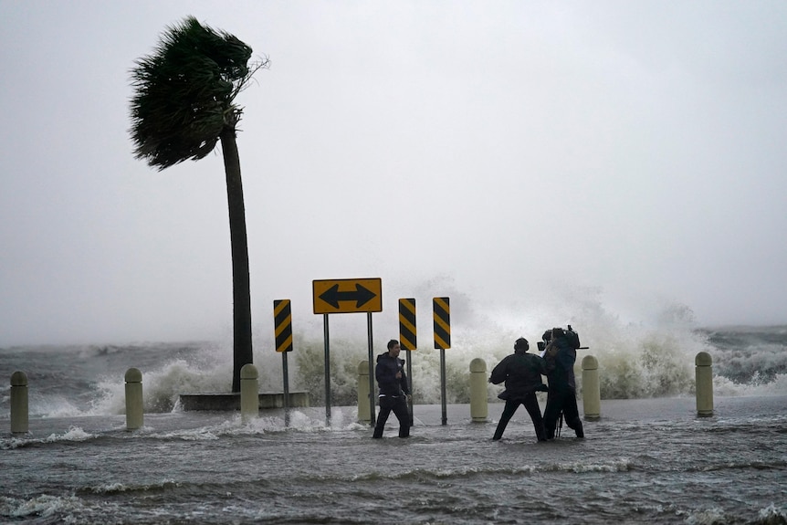 A news crew reports on the edge of a lake surrounded by water and wind caused by Hurricane Ida 