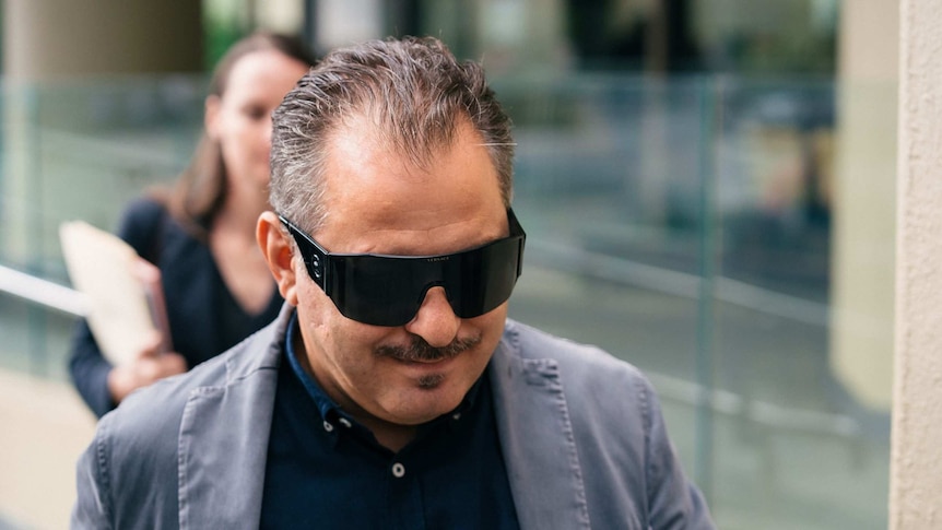 Headshot of a man wearing dark sunglasses.