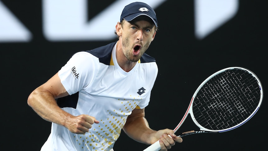 An Australian male tennis players pumps his fists as he celebrates winning a point.