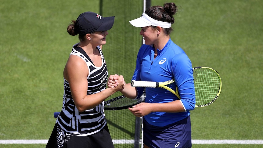Two smiling tennis players shake hands at the net after their match.