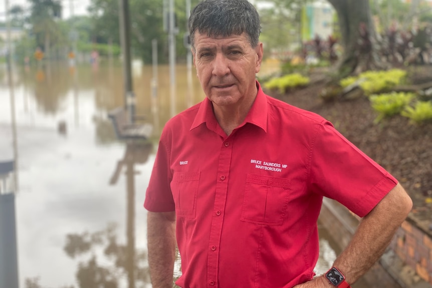 Un homme en chemise rouge se tient devant les eaux de crue.