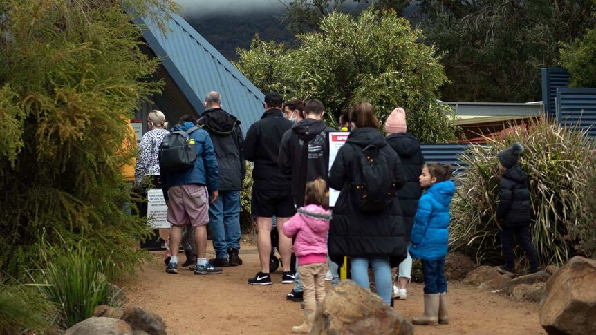 a line of people, mainly families, queues to enter a zoo