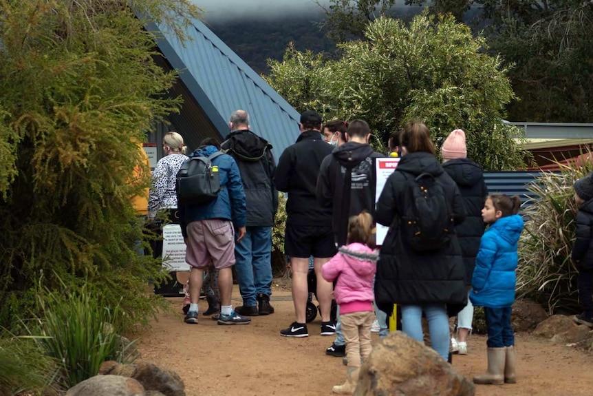 a line of people, mainly families, queues to enter a zoo