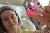 Fiona Lowenstein lying in a hospital bed with a temperature clip on her finger