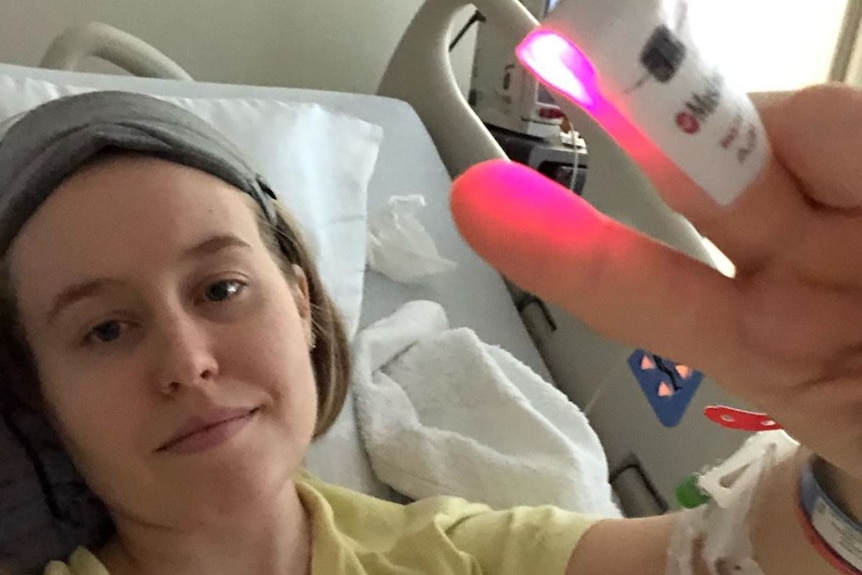 Fiona Lowenstein lying in a hospital bed with a temperature clip on her finger