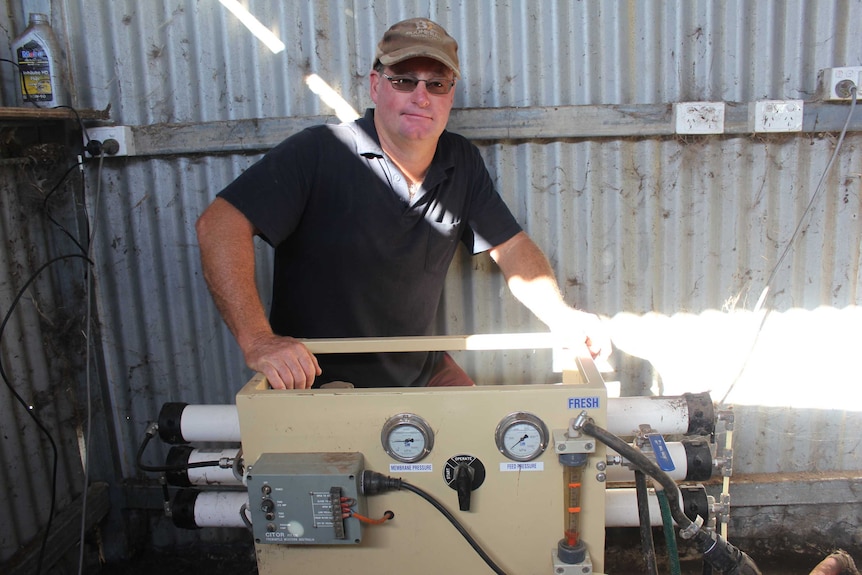 Dunn Rock farmer Doug Giles crouches down behind his desalination unit.