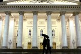 Pedestrians walk past the Bolshoi Theatre on a rainy evening in Moscow