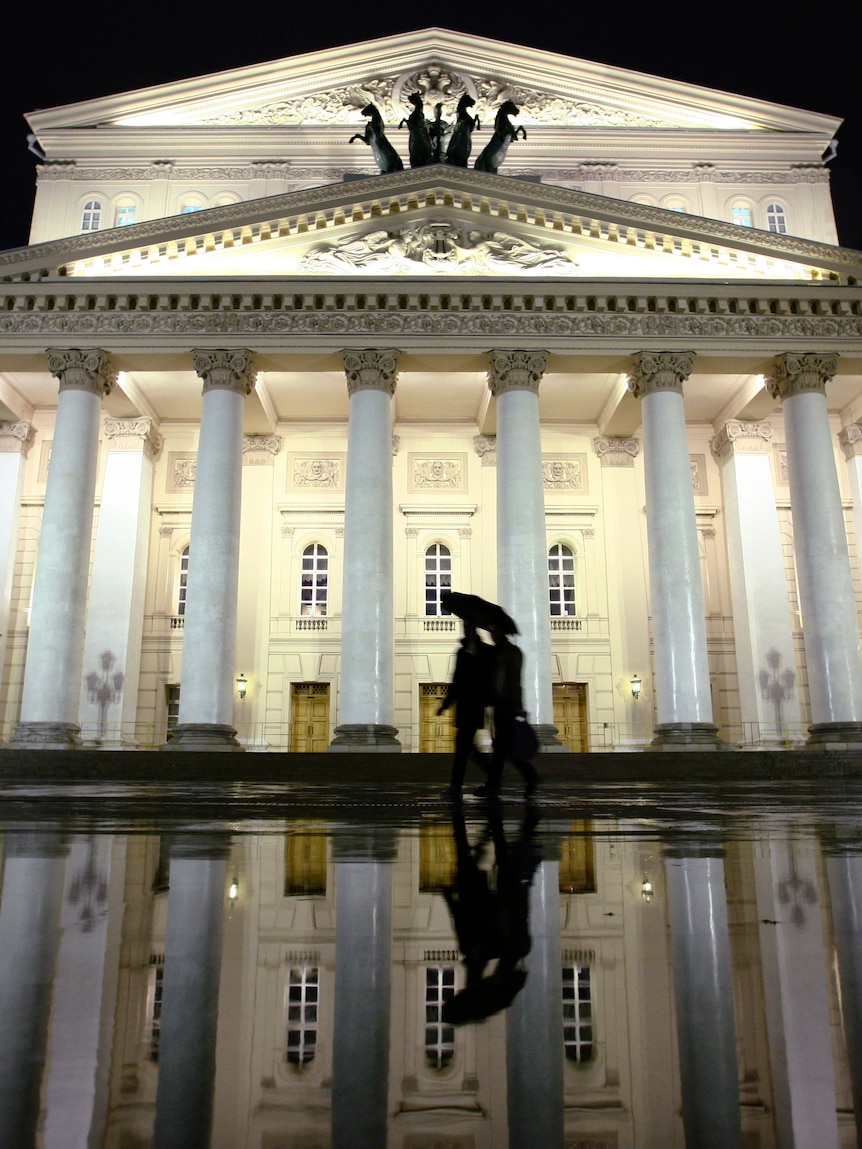 Pedestrians walk past the Bolshoi Theatre on a rainy evening in Moscow