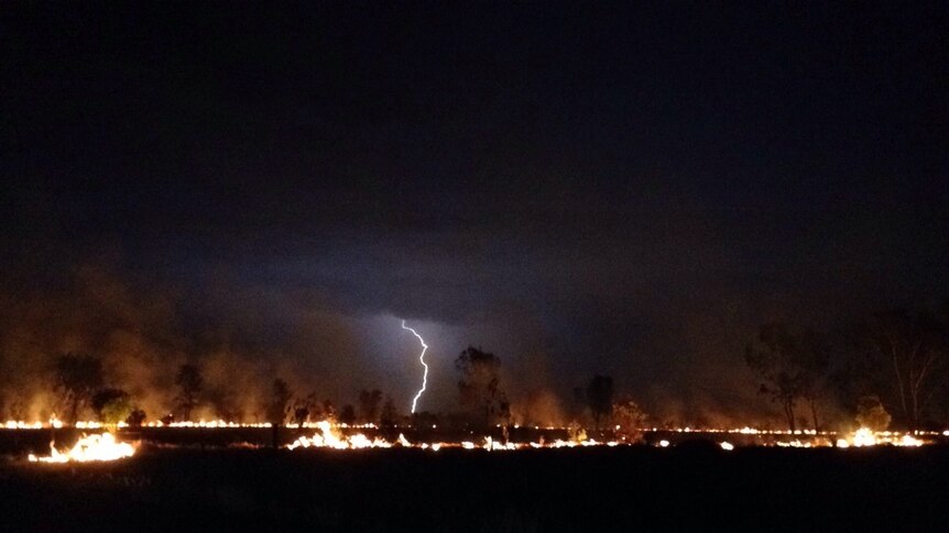 Lightning strikes the ground as a fire, started by another lightning strike, burns in the foreground.