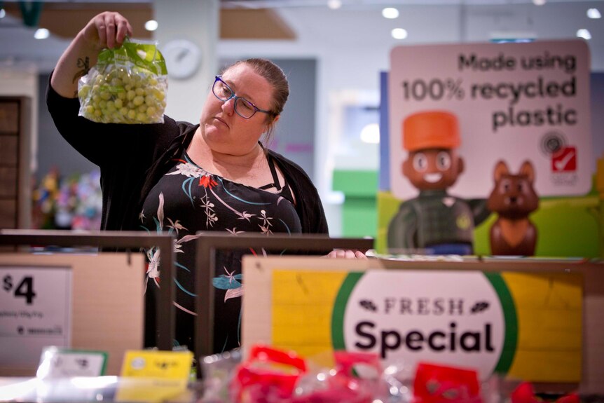 Sharmy Walker is in a supermarket. She holds a packet of grapes at head-height and inspects them.