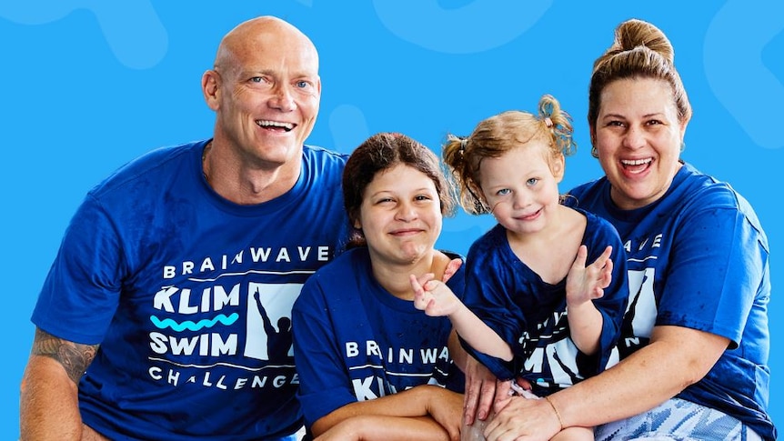 Olympian Michael Klim, a woman and two children smile at the camera wearing blue 'Brainwave Klim Swim Challenge' t-shirts.