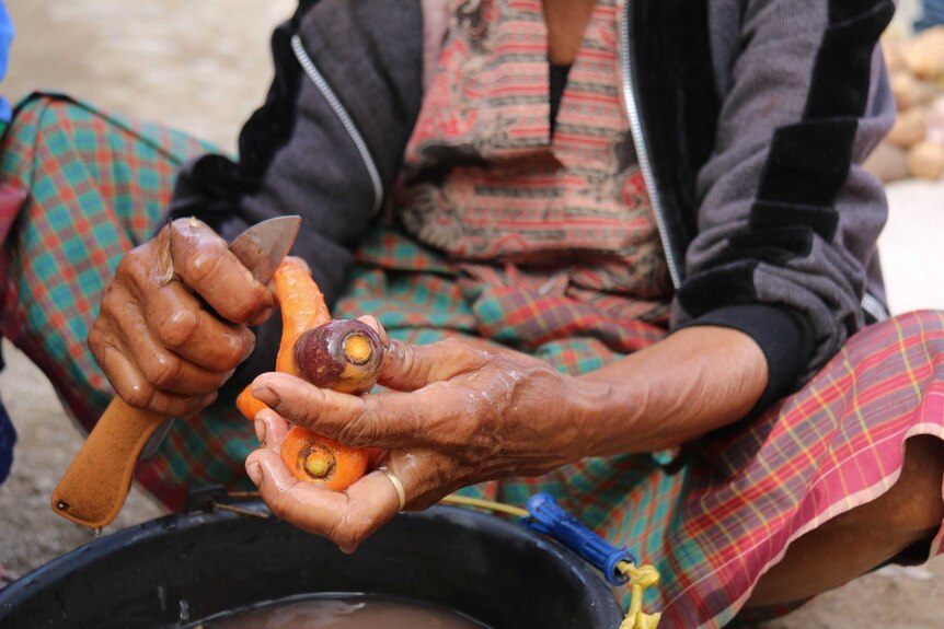 Closeup of an old woman's hands peeling carrots with a knife.
