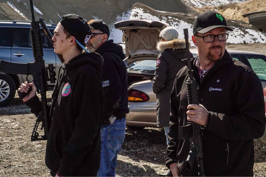 Two men wearing caps with AR-15 rifles in a snowy valley