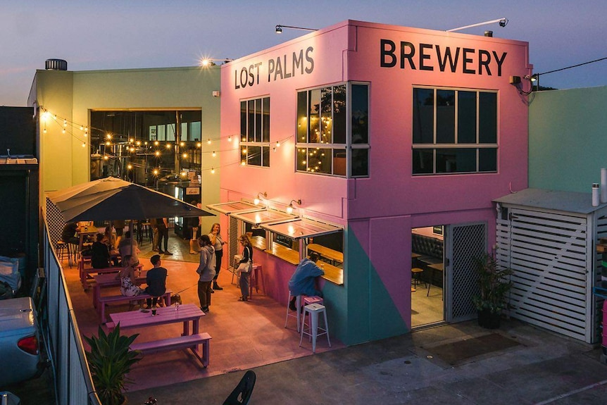 Early evening shot of a pink building with the writing that says Lost Palms Brewery. Seat with people are outside the building.