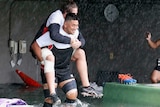 A big rugby player carries another rugby player on his back as they wade through knee-high water.
