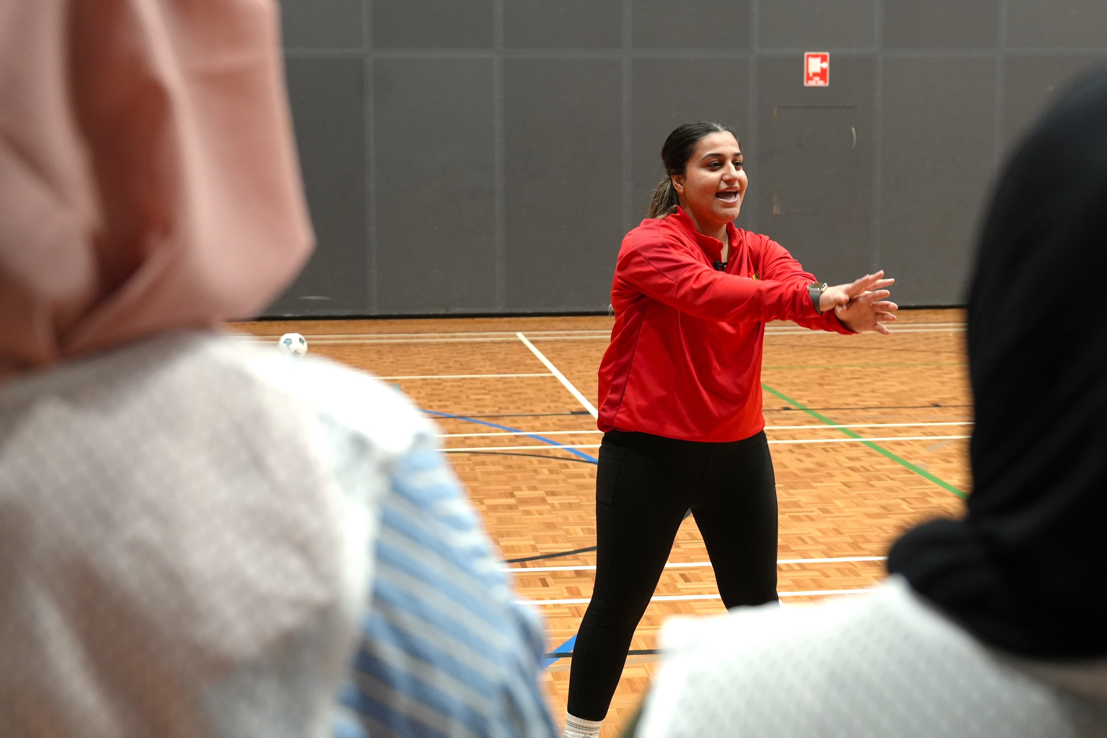 A woman wears a red jumper  while coaching on an indoor court.