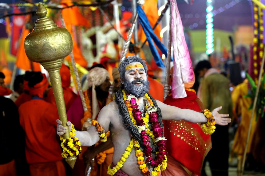 A Hindu man dances draped in flowers during Kumbh Mela