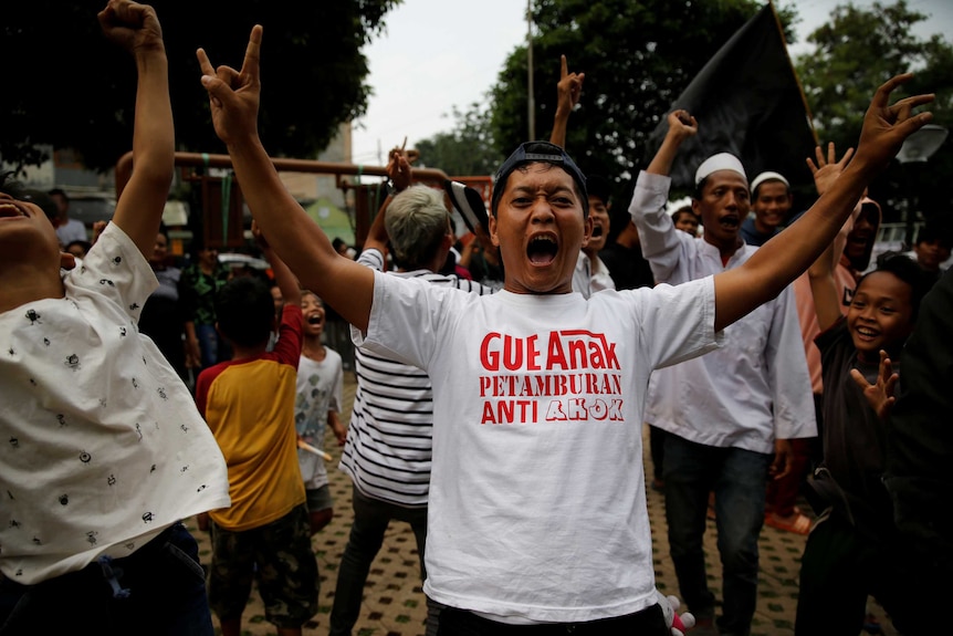 A group of men raise their hands in celebration of Anies Baswedan reported victory.