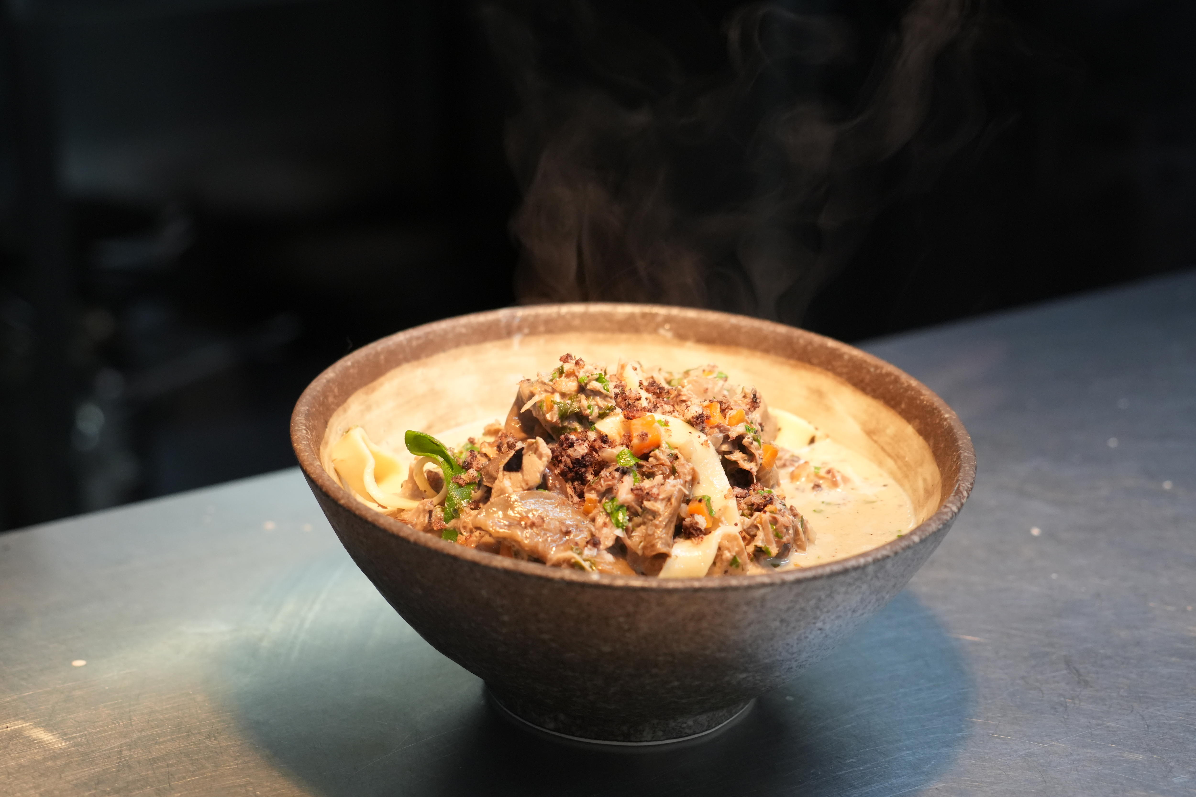 A close up of a bowl of rabbit ragu with steam rising up.