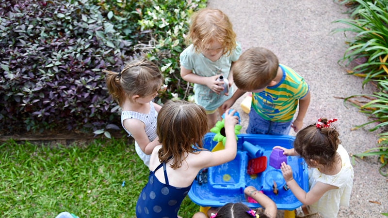 Children cluster around a water table.