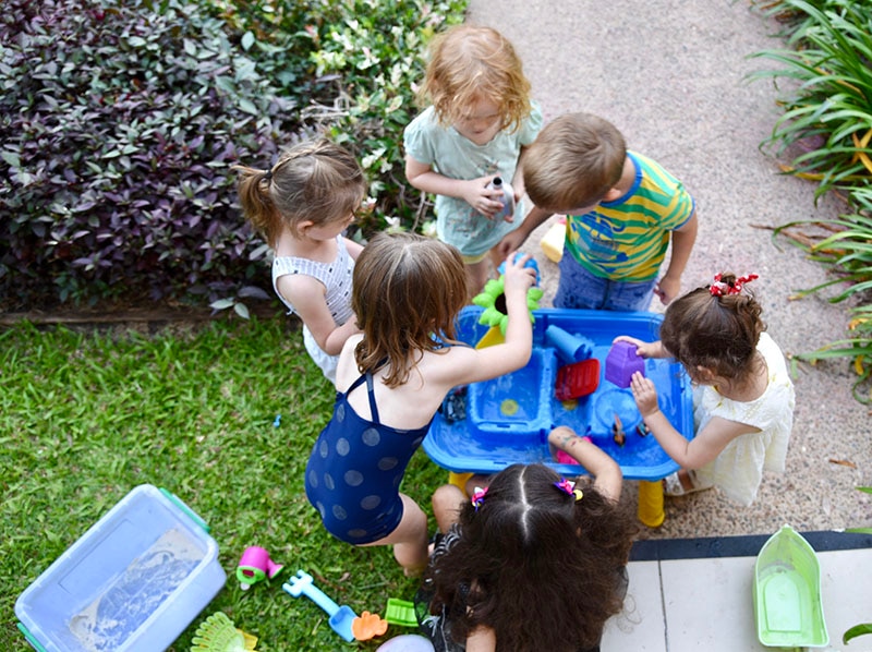 Children cluster around a water table.