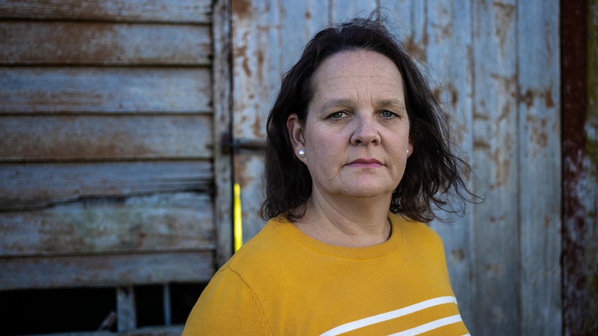 A woman wearing an orange top looks directly at the camera.