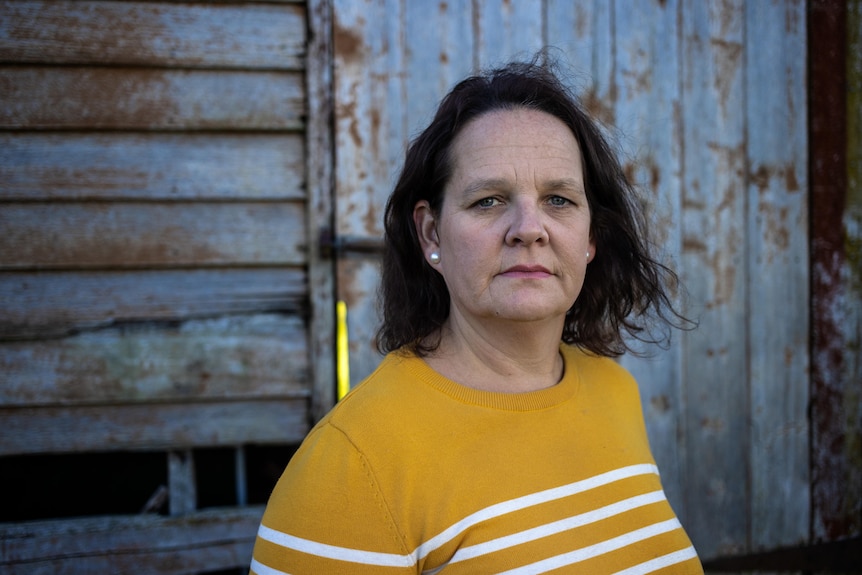 A woman wearing an orange top looks directly at the camera.