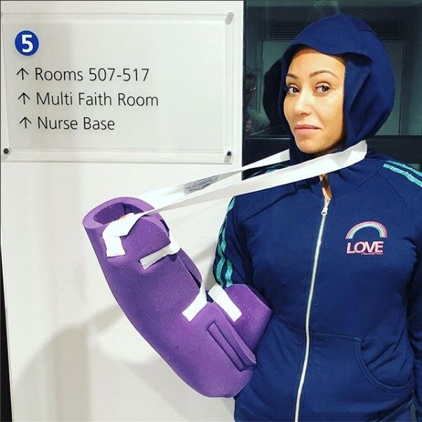 A woman in a hospital raises her right arm to display a padded cast in which it is wrapped.