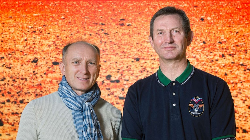 Two men stand in front of a photograph of the the Mars landscape.