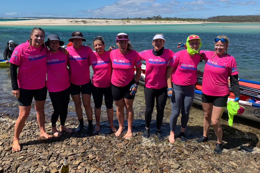 Eight women in pink jumpers stand in front of a boat