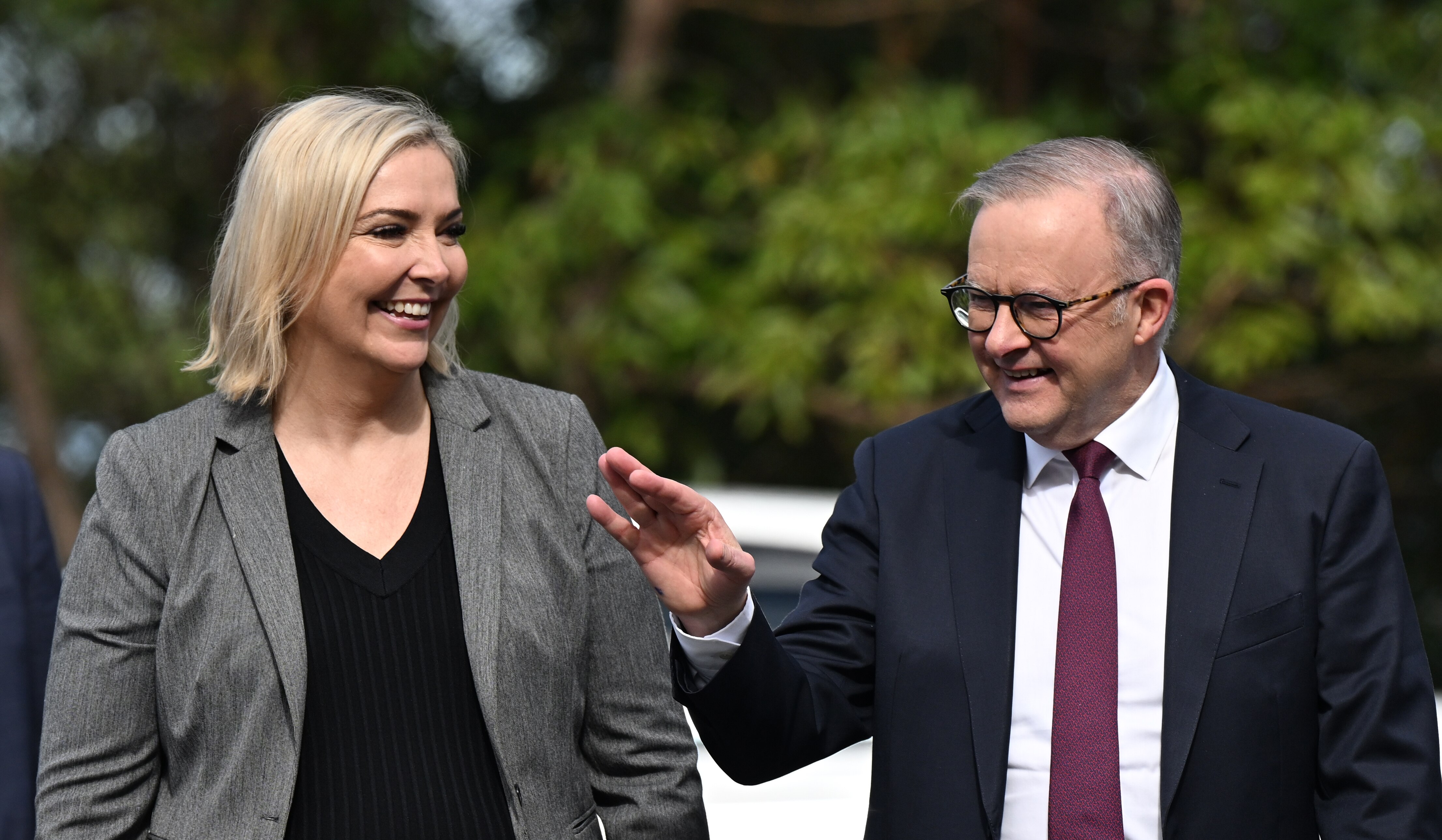 A woman in a grey jacket and Anthony Albanese walking and talking.