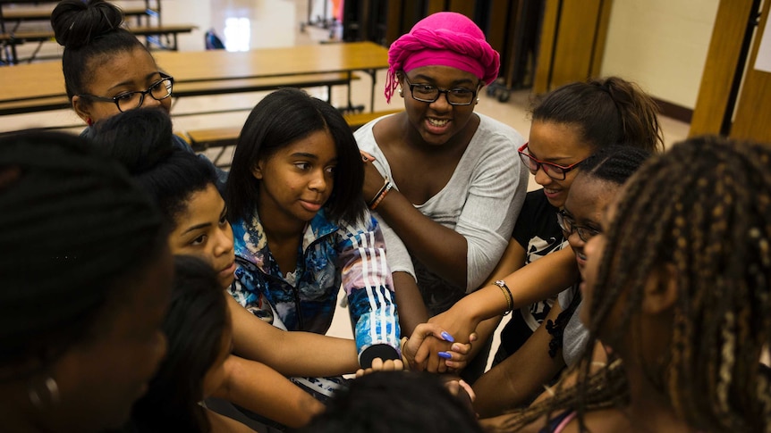 group of young women of colour, sitting on the floor, smiling and linking arms and hands