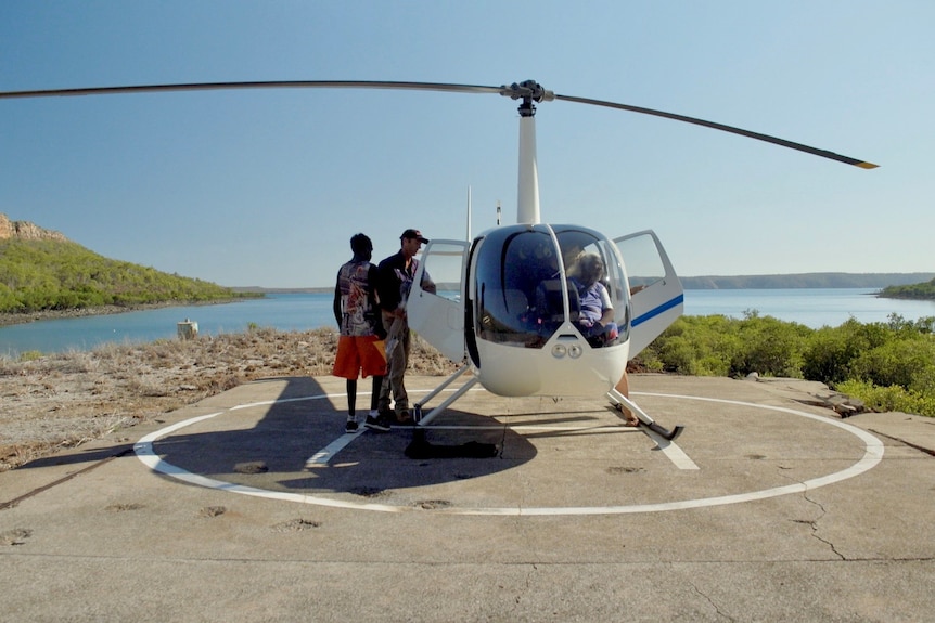 People climb into a large helicopter which is landed on a remote pad near the blue ocean