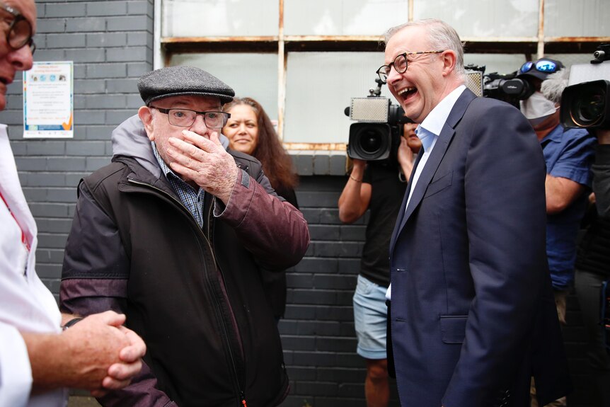 Anthony Albanese laughs next to an older man covering his mouth in surprise. 