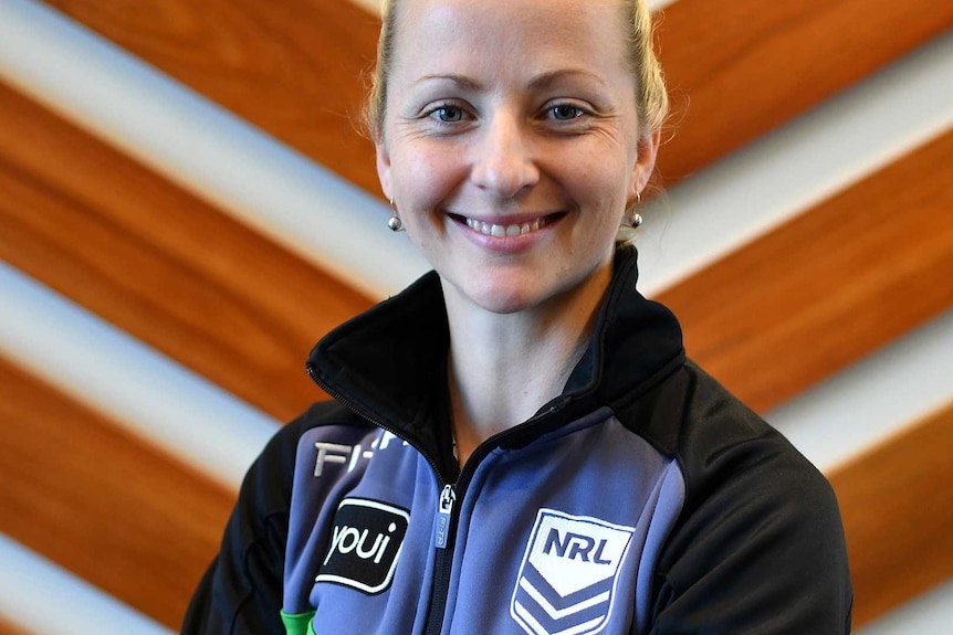 A female NRL referee looks straight at the camera while smiling and having her arms crossed.