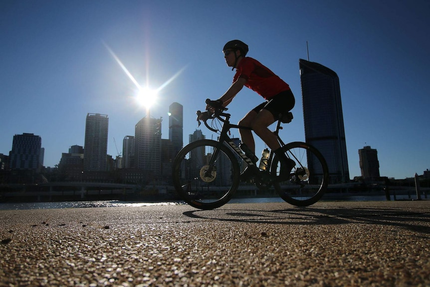 A cyclist in silhouette against a blazing sun above the Brisbane CBD