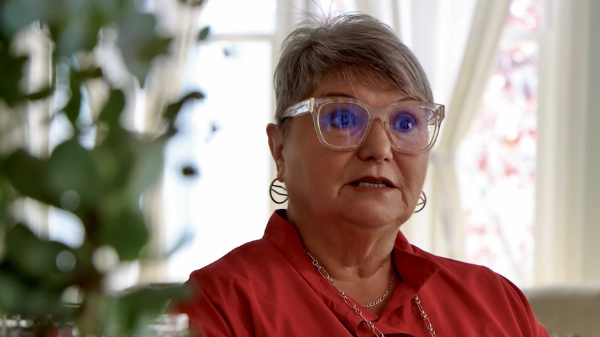 Close up of a woman, wearing glasses and a red shirt.