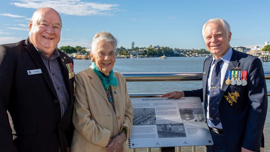 Bill Clayton, Don Currell OAM and Peggy McLellan stand in front of a plaque at the Submariners Walk Heritage Trail in Teneriffe