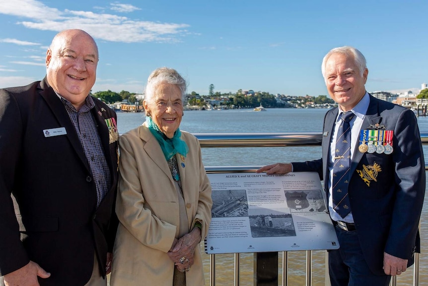 Bill Clayton, Don Currell OAM and Peggy McLellan stand in front of a plaque at the Submariners Walk Heritage Trail in Teneriffe
