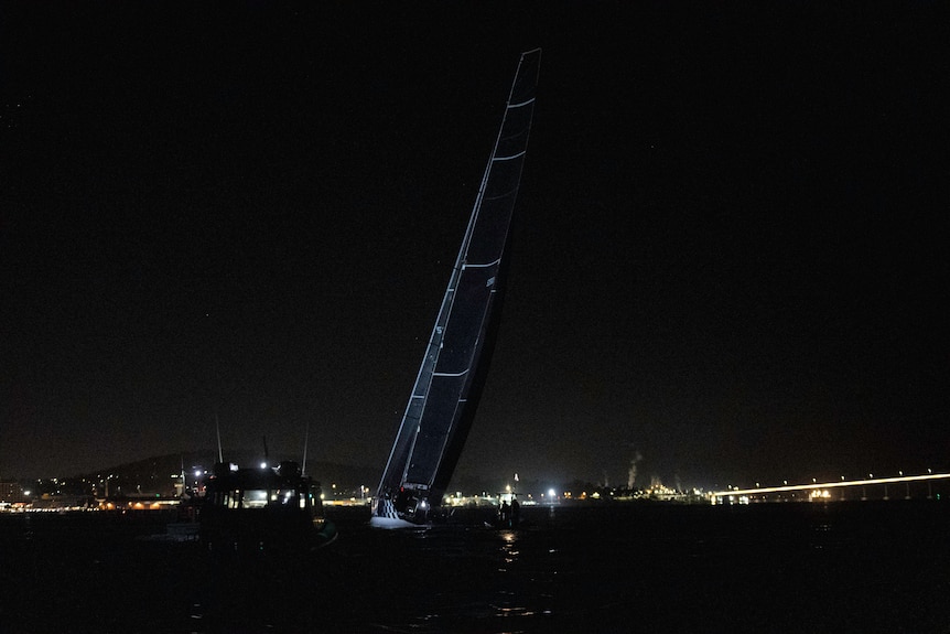 A yacht with black sails on a river at night.