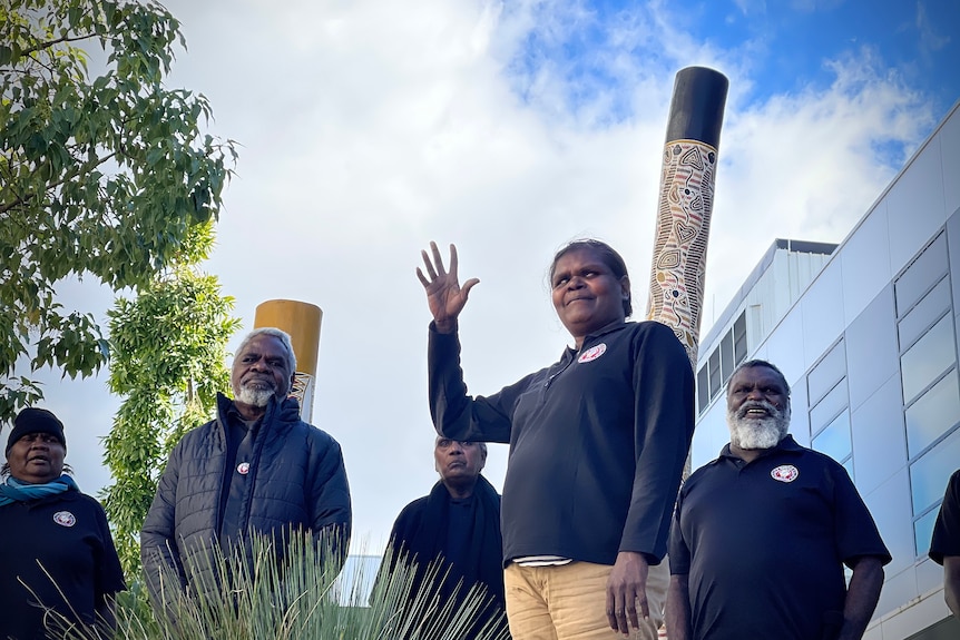 A group of Galiwin’ku community members stand smiling around a tall wooden pole.