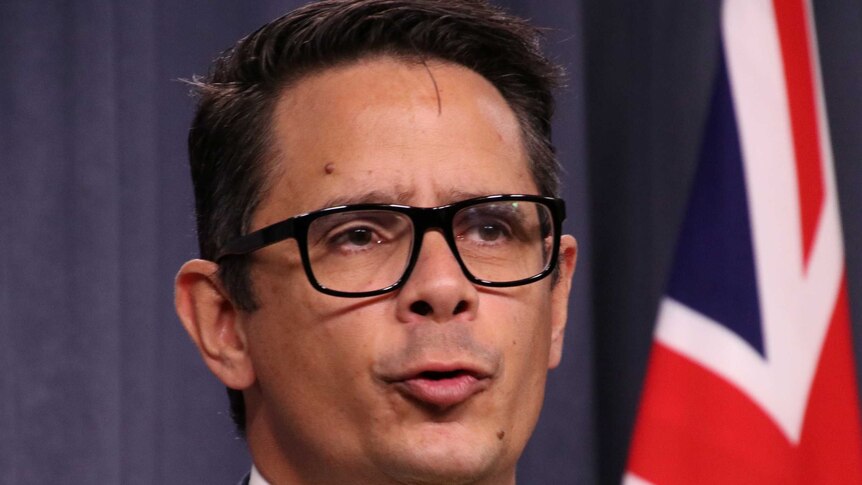 Headshot of Ben Wyatt, wearing glasses, with Australian flag in background.